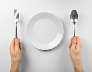 Male hands holding silver cutlery near plate, isolated on white