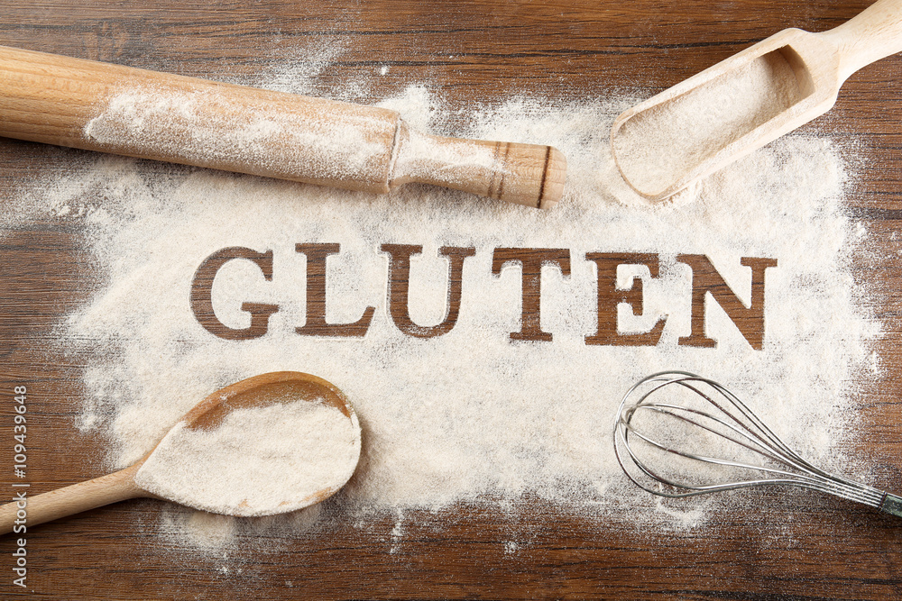 The word GLUTEN from flour on wooden table, top view