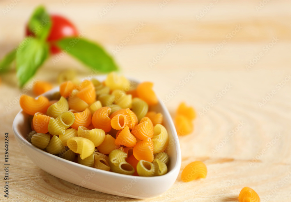 Dry multicolored gomiti pasta in white bowl on wooden table