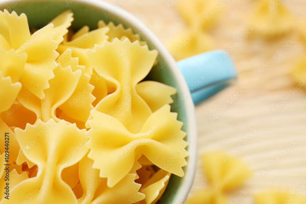 Dry farfalle pasta in blue cup on wooden table