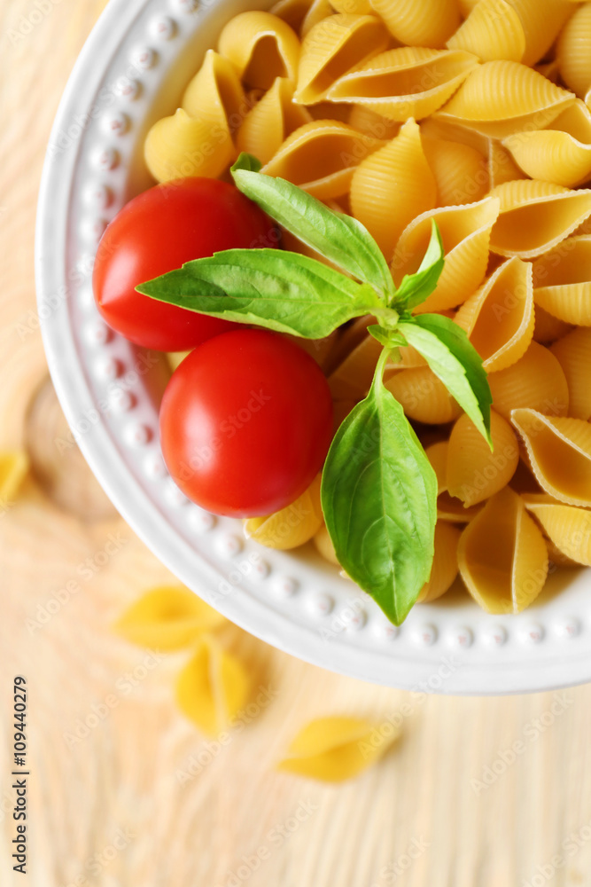 Dry conchiglie pasta in white plate on wooden table