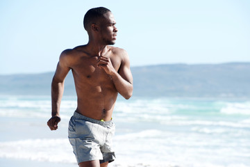 Wall Mural - Muscular young man running along the beach