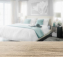 Wooden Table Top With Blur Of Cozy Bedroom Interior With White And Green Pillows On Bed