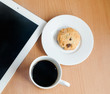 Coffee, cookies and tablet placed on a wooden table.