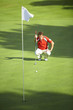 © Connect Images - Front view of golfer crouching down in front of golf flag considering strategy