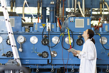 Young Woman Wearing Lab Coat Holding Digital Tablet, Looking Up At Scientific Equipment Smiling