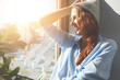 © WHstudio Leushin N - Happy young female artist contemplating urban landscape through the window, smiling in delight while relaxing on the windowsill after finishing drawing another masterpiece. Flare sun, film effect