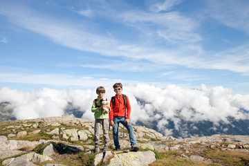 two boys stand on top in high mountain next to the clouds