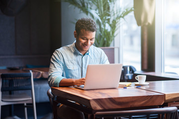 Attractive male worker is using computer in cafeteria 