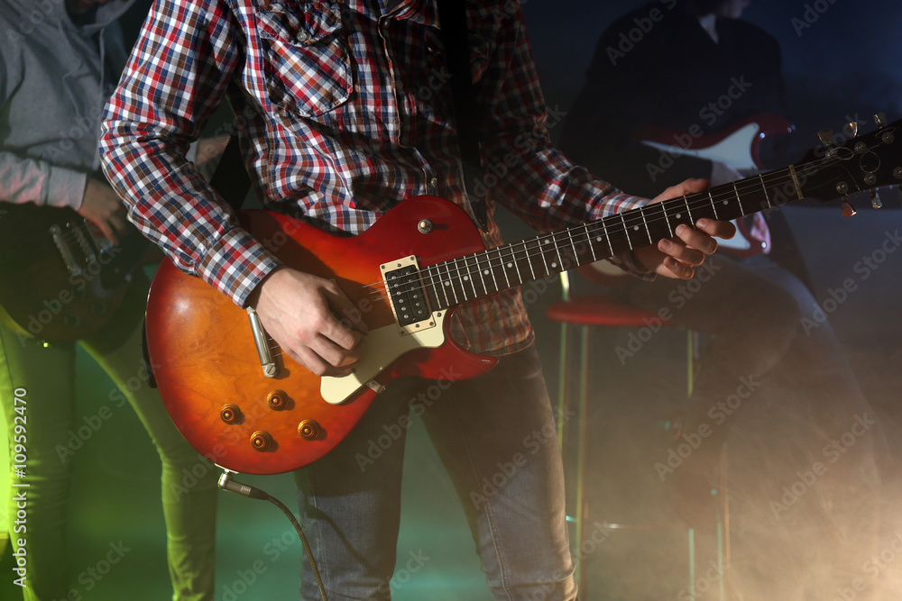 Young group playing electric guitar on lighted foggy background