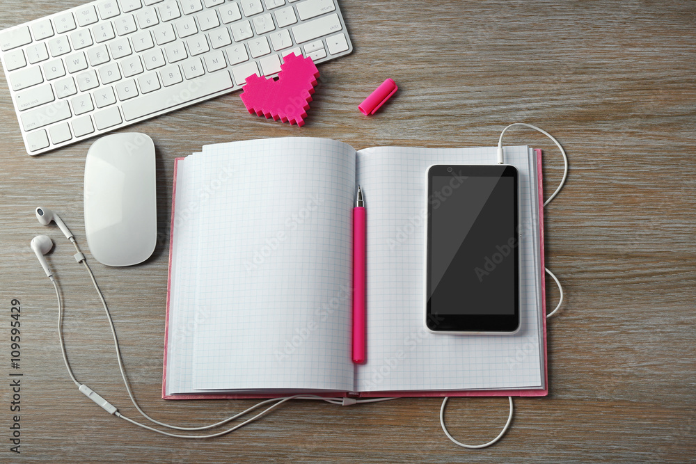 Computer peripherals with pink heart, notebook and mobile phone on wooden table