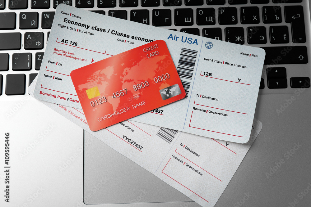 Laptop with credit card and flight tickets on light wooden table