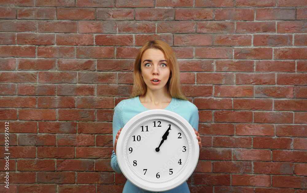 Young beautiful woman holding clock against brick wall background
