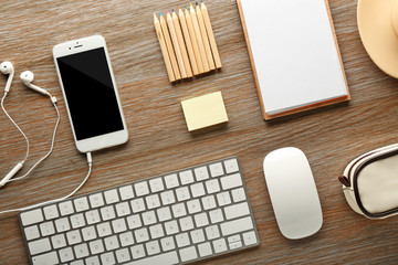 Workplace with mobile phone, peripheral devices and stationery on wooden table