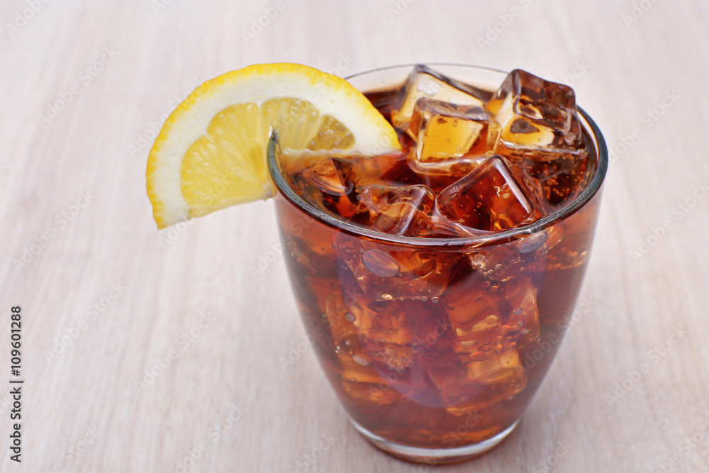 Glass of cola with ice on light wooden background