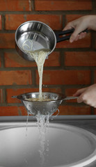 Wall Mural - Female hands pouring water from boiled spaghetti over sink in the kitchen