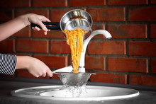 Female Hands Pouring Water From Boiled Pasta Over Sink In The Kitchen