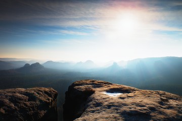 Blue spring daybreak. Sandstone cliff above deep misty valley in Saxony Switzerland. Hilly peaks