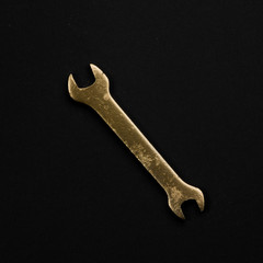 Golden wrench isolated on black background. Symbolic repair tool