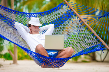 Young man with laptop at hammock on tropical vacation