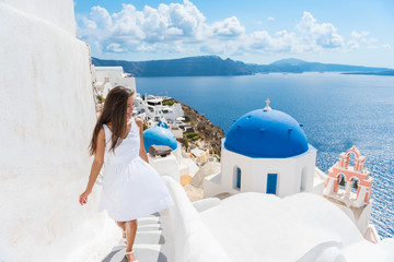 Fototapete - Santorini travel tourist woman on vacation in Oia walking on stairs. Person in white dress visiting the famous white village with the mediterranean sea and blue domes. Europe summer destination