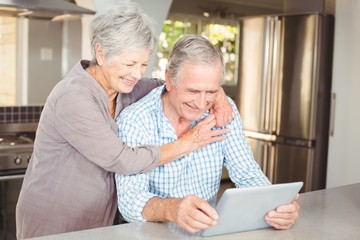 Wall Mural - Happy senior woman embracing man using tablet