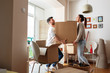 Young married couple carrying big cardboard box into new home. Moving house.	