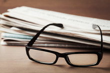 Eyeglasses And Stack Of Newspapers On Wooden Desk For Themes Of Ophthalmology, Poor Vision And Reading