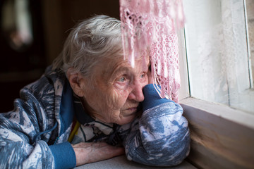 Wall Mural - An elderly woman sadly looking out the window.