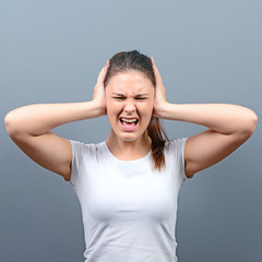 Portrait of woman covering ears with hands against gray backgrou