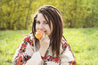 Pretty young woman with dreadlocks. Young woman in folk dress with dreadlocks eating an apple and smiling. Green grass background.
