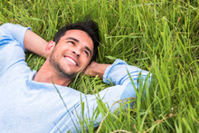 Happy Beautiful Young Man On The Green Grass Dreaming And Look Up, At The Sky. Relax