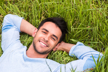 Happy beautiful young man lying on the green grass dreaming and look at the camera. Relax