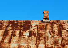 Old Rusty Metal Roof With Brick Chimney Against Blue Sky Background
