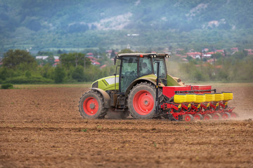 Fototapete - Farmer in tractor sowing crops at field with seed scattering agr