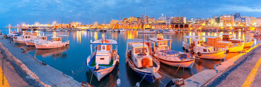 Obraz na płótnie Panorama of Old harbour with fishing boats and marina during twilight blue hour, Heraklion, Crete, Greece. Boats blurred motion on the foreground. w salonie