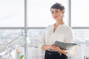 Close-up portrait of a young confident female office manager at her workplace, ready for doing business task.