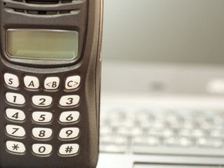 Closeup of black portable radio communication with blurred keyboard in background.