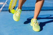Sports Athlete Picking Up Ball With Tennis Racket. Female Player Using A Technique With Her Running Shoes To Pick Up During Game On Blue Hard Court. Closeup Of Feet, Neon Yellow Fashion Footwear.