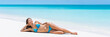 Caribbean turquoise ocean getaway beach destination lady dreaming on perfect white sand. Paradise tropical travel destination. Asian blue bikini woman lying down relaxing sun tanning laid back.