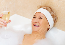 Senior Woman Relaxing In Bath With Glass Of Champagne