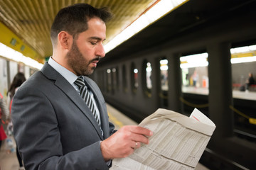 Man reading a newspaper while waiting for the subway train