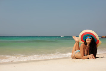 Wall Mural - Young girl in big hat lung on sea beach. Summer, sun, vacation and travel. Enjoy of Freedom