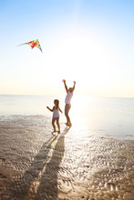 Happy Young Father With Daughter With Flying A Kite On The Beach