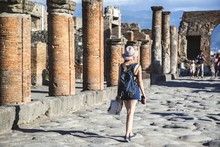 Young Woman Tourist, From The Back, Walking In The Ruins Of Pompeii