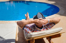 Man In Hat Sunbathing On A Sun Lounger By The Pool