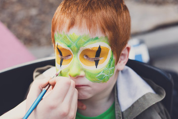 Child face painting process at redhead boy