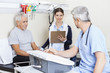 © Tyler Olson - Physiotherapist Holding Clipboard While Colleague And Patient Si