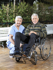 Canvas Print - Physiotherapist Crouching By Senior Man In Wheelchair At Lawn