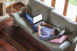 © GENETTICA - Young man lying comfortably on the sofa while using the laptop w